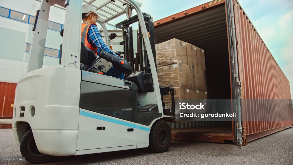 Forklift Driver Loading a Shipping Cargo Container with a Full Pallet with Carboard Boxes in Logistics Operations Port Terminal. Forklift Stock Photo