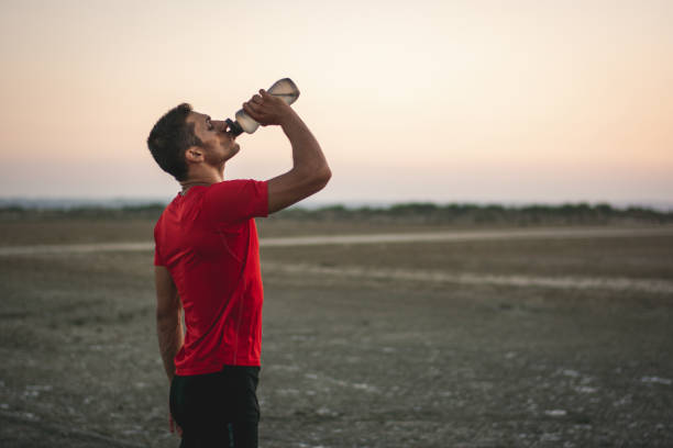 Fit man drinking water and resting after exercising in nature Tired sporty man drinking energy drink and relaxing after training and working out in nature sport drink stock pictures, royalty-free photos & images