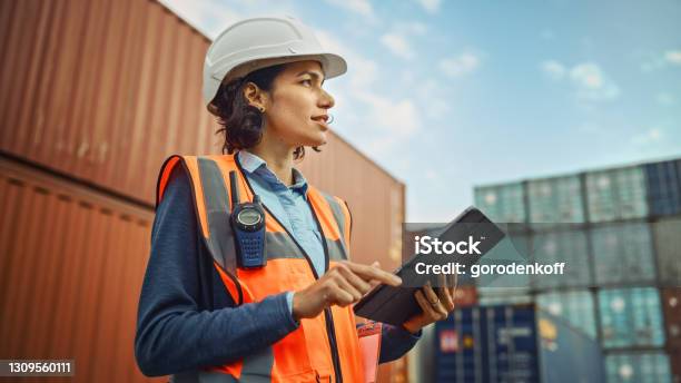 Smiling Portrait Of A Beautiful Latin Female Industrial Engineer In White Hard Hat Highvisibility Vest Working On Tablet Computer Inspector Or Safety Supervisor In Container Terminal Stock Photo - Download Image Now