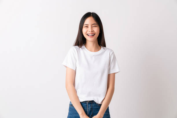 estudio de la hermosa mujer asiática alegre en camiseta blanca y de pie sonriendo con frenos en el fondo blanco. - banda correctora fotografías e imágenes de stock