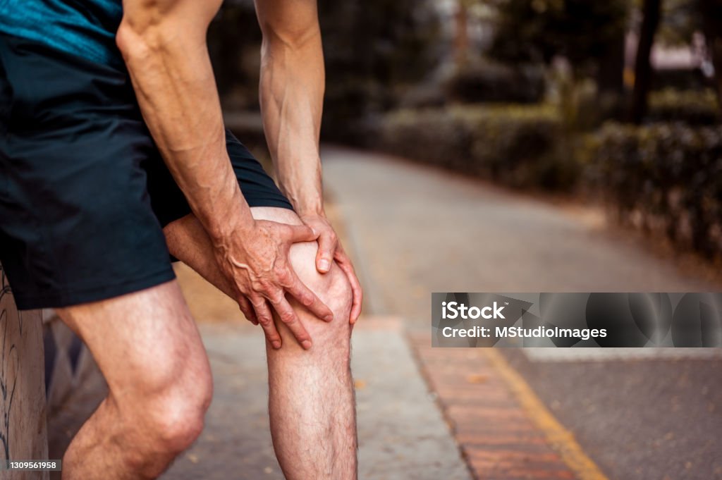 The athlete holds on to his knee as he feels pain Pain Stock Photo