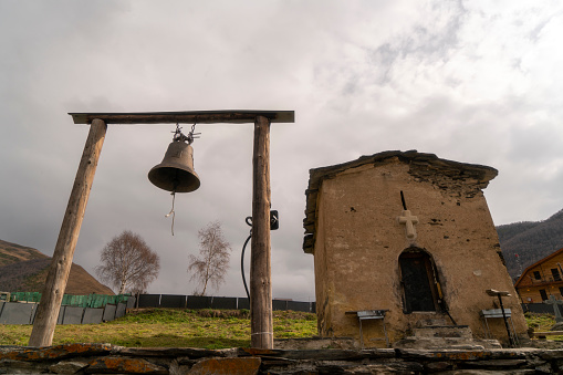 A church bell hanging a wooden pile with small church in Georgia.