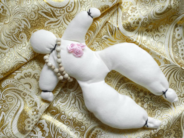 Close-up of white cloth voodoo doll with wooden chain and pin with pink roses, to be used in a love ritual.