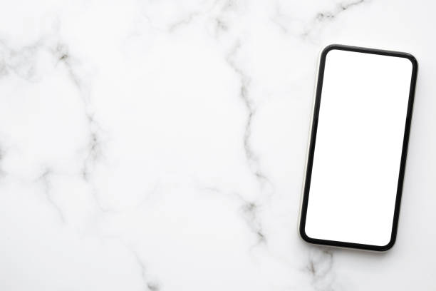 istock Smartphone with white blank mock up screen is on top of white marble desk table. Top view with copy space, flat lay. 1309566937