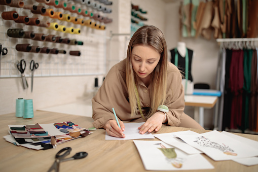 woman fashion designer draws sketches. attractive young female dressmaker or tailor sketching in studio. Small business concept