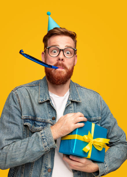istock Funny bearded guy with birthday present blowing party horn 1309569233