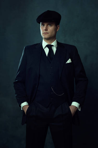uomo vintage in abito a strisce scure e berretto di fronte a parete scura. - 20s businessman suit people foto e immagini stock