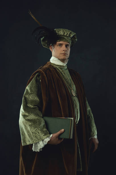 istock Renaissance man holding a book stands in front of a dark wall. 1309571664