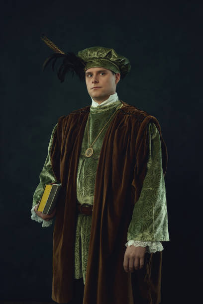 istock Renaissance man holding a book stands in front of a dark wall. 1309571666