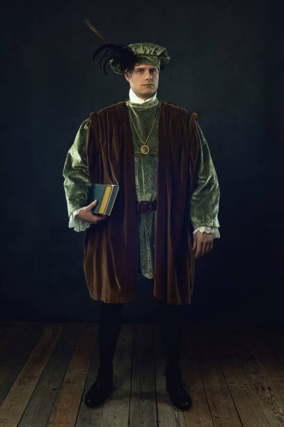 istock Renaissance man holding a book stands in front of a dark wall. 1309571668