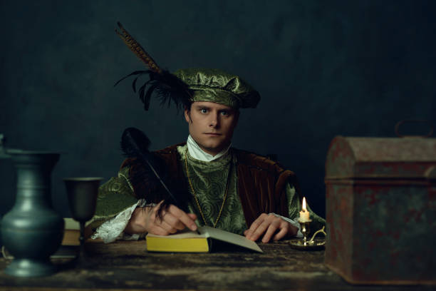 istock Renaissance man sits behind table writing in a notebook by candlelight in the evening. 1309571678