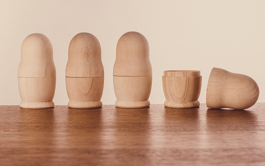 Four unpainted nesting dolls in a row, three closed, one open. Soft brown colors, wooden materials.