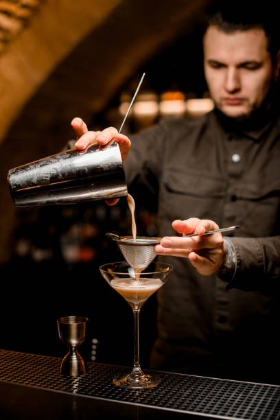 istock man bartender holds sieve and pours cocktail through it from shaker into glass 1309576058