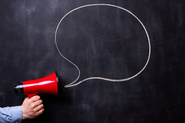 istock Man holding red loudspeaker in front of a blackboard. There is a hand drawn message bubble. 1309576203