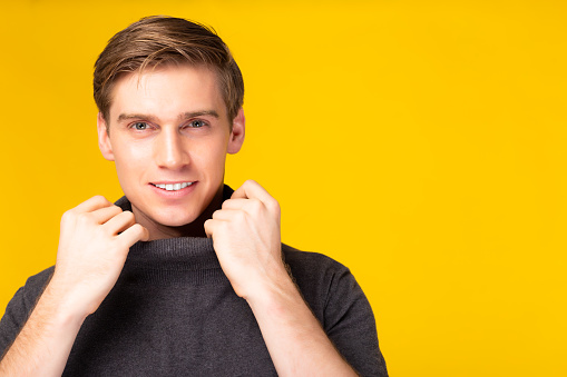 Happy young handsome caucasian man portrait with holding collar sweater Studio shot isolated on yellow background Attractive handsome guy get confident and look charming Fashion and hairstyle concept