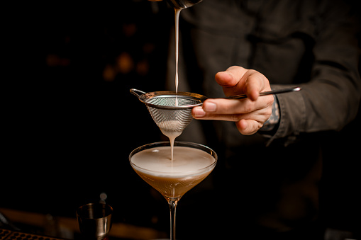 vista de primer plano sobre el tamiz a través del cual el camarero macho vierte cóctel de martini espresso espumoso en vidrio photo
