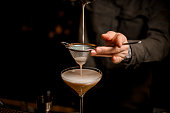 close-up view on sieve through which male bartender pours frothy espresso martini cocktail into glass