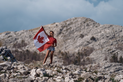 Child teenager girl holding a Canada flag on of the mountain