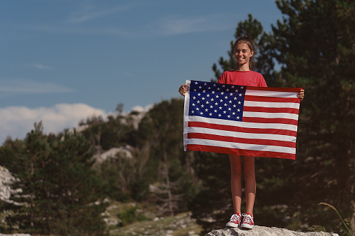 Child teenager girl holding an American flag at nature background. USA resident, US citizen. Immigration concept.