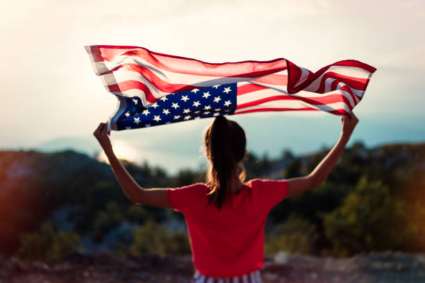 ragazza adolescente sta sventolando bandiera americana in cima alla montagna sullo sfondo del cielo - child flag fourth of july little girls foto e immagini stock