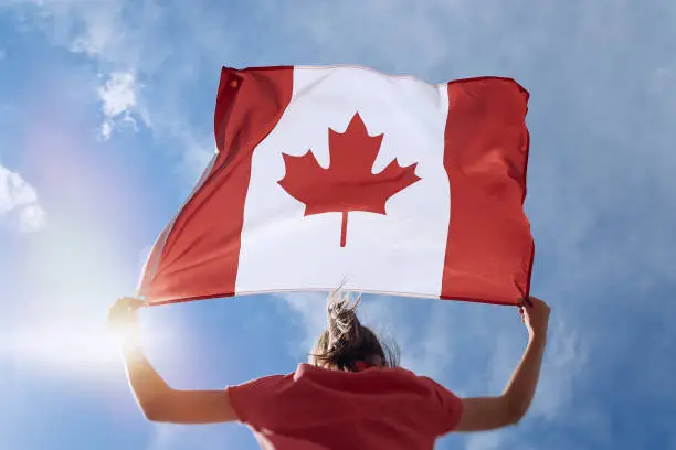 Child girl is waving Canadian flag on top of mountain at sky background