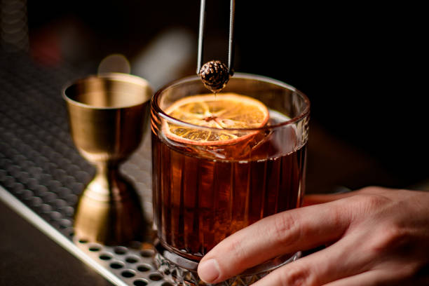 close-up view on glass with cocktail decorated with orange slice and small pine cone close-up view on old-fashioned glass with cold alcoholic cocktail decorated with orange slice and small pine cone glass of bourbon stock pictures, royalty-free photos & images