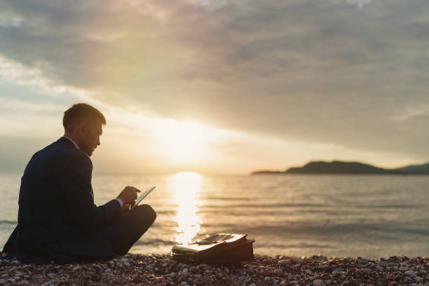 istock Businessman in a suit using tablet while sitting of the beach 1309580461