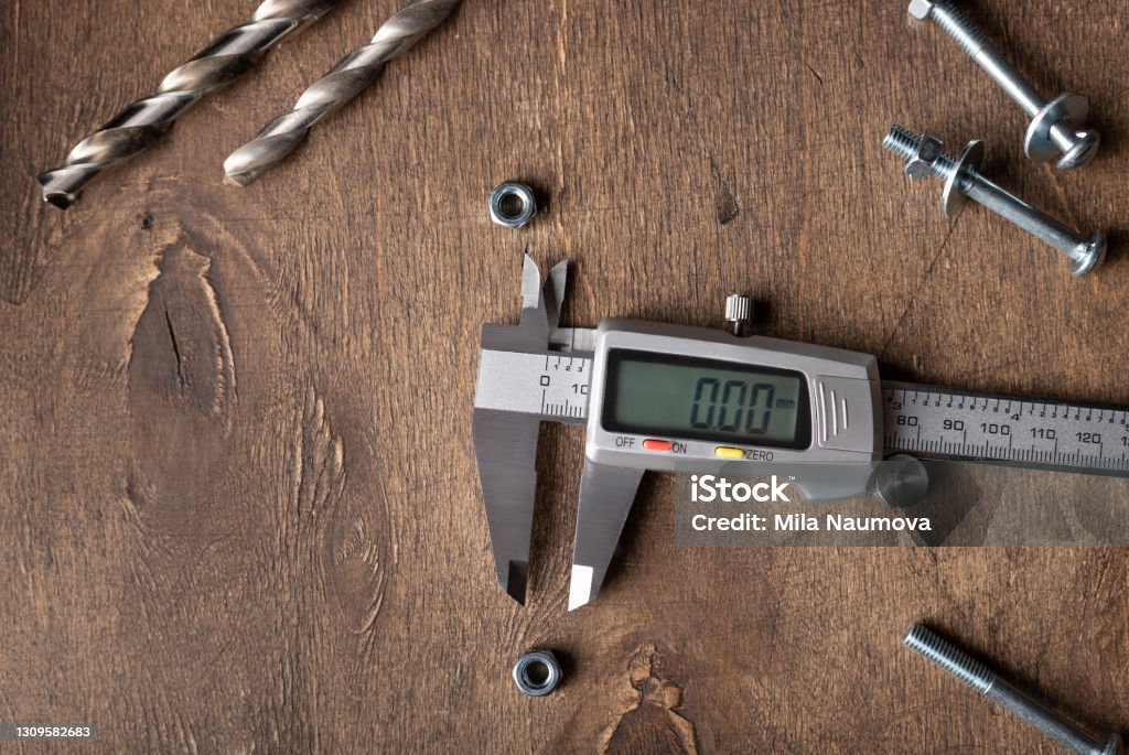 Digital caliper on wooden table with hardware Digital vernier caliper on wooden table with hardware. Measuring accessories. top view. copy space Caliper Stock Photo