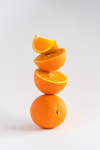 Close-up of a stack of oranges, whole and sliced, a tower of oranges on white background with copy space, vertical