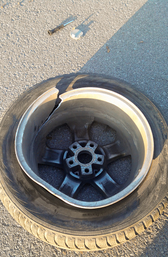 On the asphalt close-up lies a wheel from a car with a split alloy wheel, smashed in a hole on the road