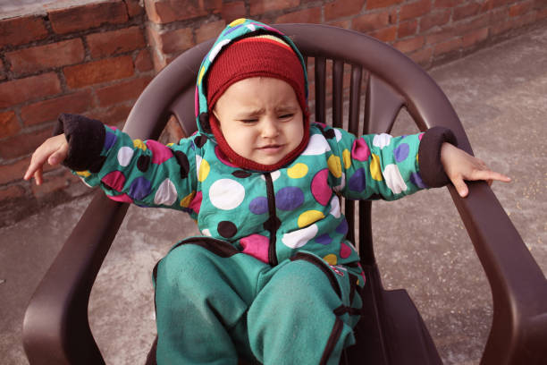 Small baby sitting on plastic chair on rooftop at home.