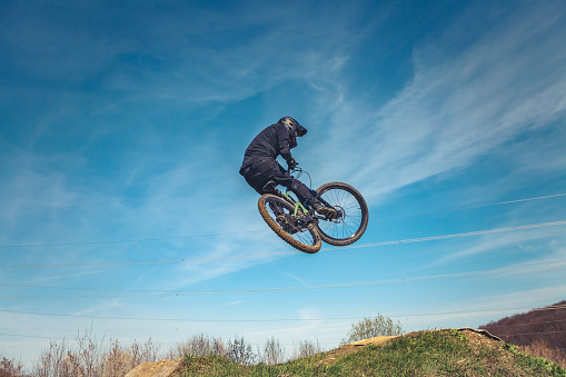 back view of man doing midair stunts with mountain bike out in the nature on trails.