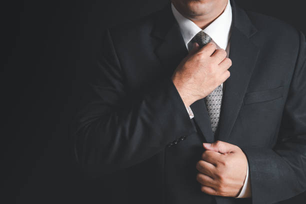 istock businessman with black suit adjusting his necktie on black background, 1309588801