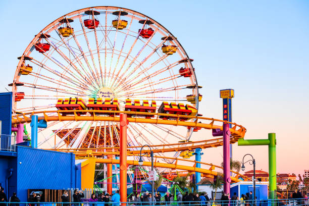 ruote panoramica e montagne russe al molo pacific park al tramonto con persone che cavalcano le attrazioni - santa monica beach los angeles county city of los angeles foto e immagini stock