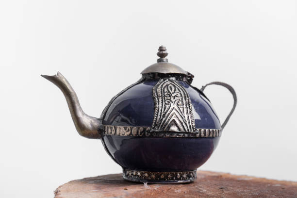 closeup of a blue metallic teapot with Moroccan motifs on a wooden surface, the background is white