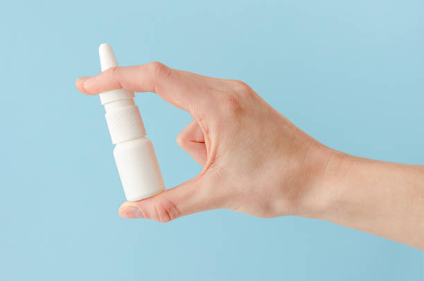 Female hand holding nasal spray Female hand holding nasal spray on blue background. Seasonal allergy and common cold concept. nasal spray stock pictures, royalty-free photos & images