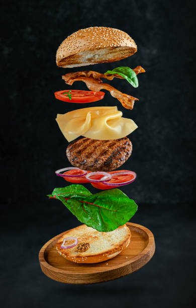 Flying hamburger Flying hamburger with ingredients on dark stone background. Creative still life bacon cheeseburger stock pictures, royalty-free photos & images