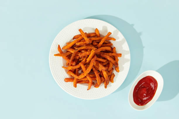 batata doce frita e molho em fundo azul com sombras longas em estilo mínimo - sweet potato french fries yam baked - fotografias e filmes do acervo