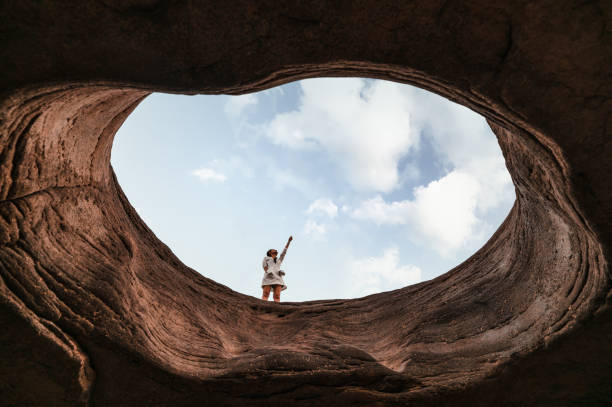 istock Young asian woman standing on hole cave and pointing at blue sky at Sam Phan Bok 1309602874