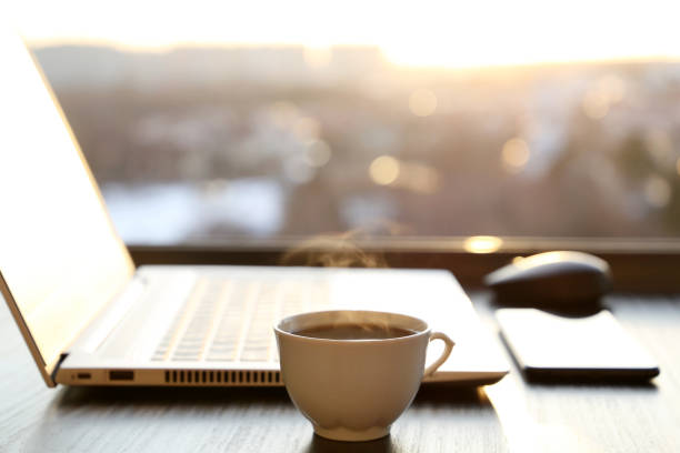istock Cozy workplace in home office with coffee cup, laptop and smartphone on table against the window at sunset 1309602949