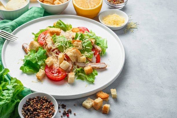 istock Caesar salad close-up on a white plate surrounded by ingredients on a gray background 1309603170