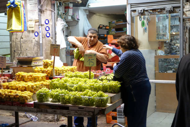 Jerusalem, Israel - December 21, 2018: Colourful fruit and vegetables displayed on a stall in Machane Yehuda Market in the evening,  Jerusalem, Israel. Some unidentified people in the background.