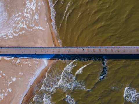 Aerial top view of the bridge to the sea from coastline leading to the Baltic sea. Pedestrians bridge in Palanga, next to ruins of old historic bridge among the waves