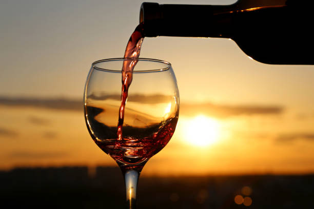 Red wine pouring from a bottle into the glass on beautiful sunset background