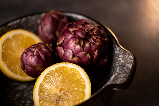 Close up on purple artichoke with lemon in a black pot.