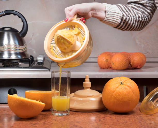 Female hand pouring orange juice into glass. Closeup on womenâs hand making fresh orange juice. stock photo