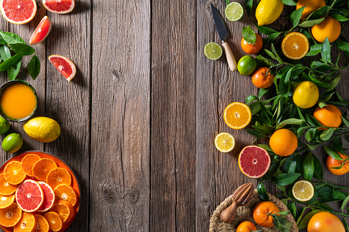 Citrus fruit arrangement with oranges, lemons, tangerine and grapefruit slices half cut and orange tree branches and leaves on rustic wooden table board