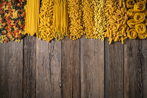 Assorted italian pasta raw uncooked on wooden rustic background with spaghetti, tagliatelle, penne, fusilli, farfalle, tortellini, tortiglioni