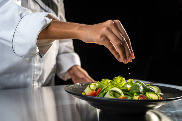 istock Chef adjusting final taste of meal before serving. Salting mixed fresh vegetable salad. 1309616389