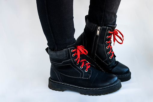 Women's feet in black shoes with red laces on a thick sole on a white background.